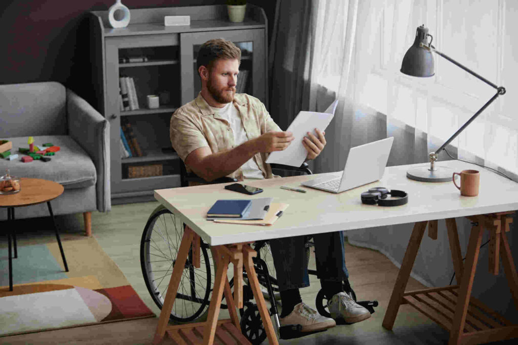 Man in wheelchair reviewing disability insurance claim documents at home office desk with laptop, highlighting importance of careful disability insurance appeal process