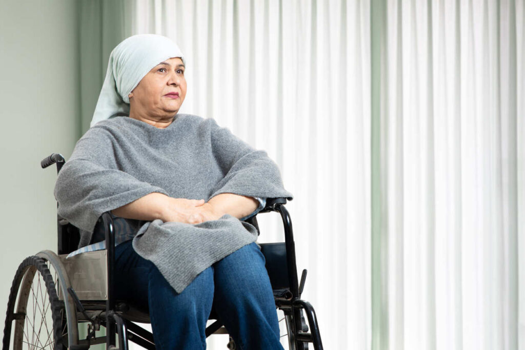 A woman wearing a headscarf sits in a wheelchair with a pensive expression, symbolizing the ongoing challenges and persistent side effects faced by cancer survivors when pursuing disability claims.