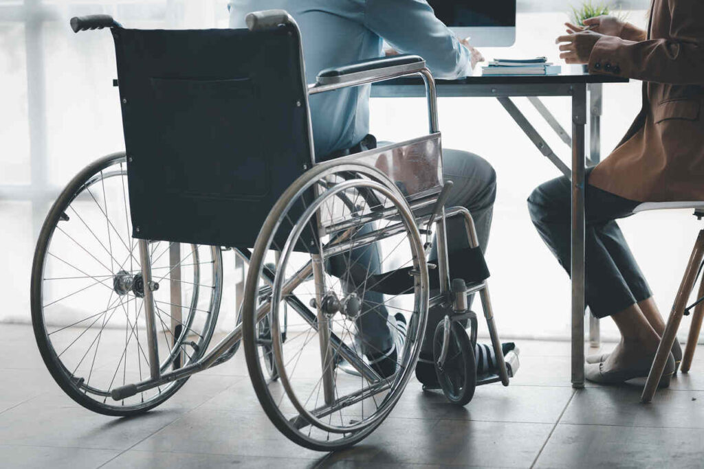 A business owner in a wheelchair works at an office desk with another professional, illustrating the complexities of proving partial disability and the challenges faced by high-income professionals beyond just an income drop.