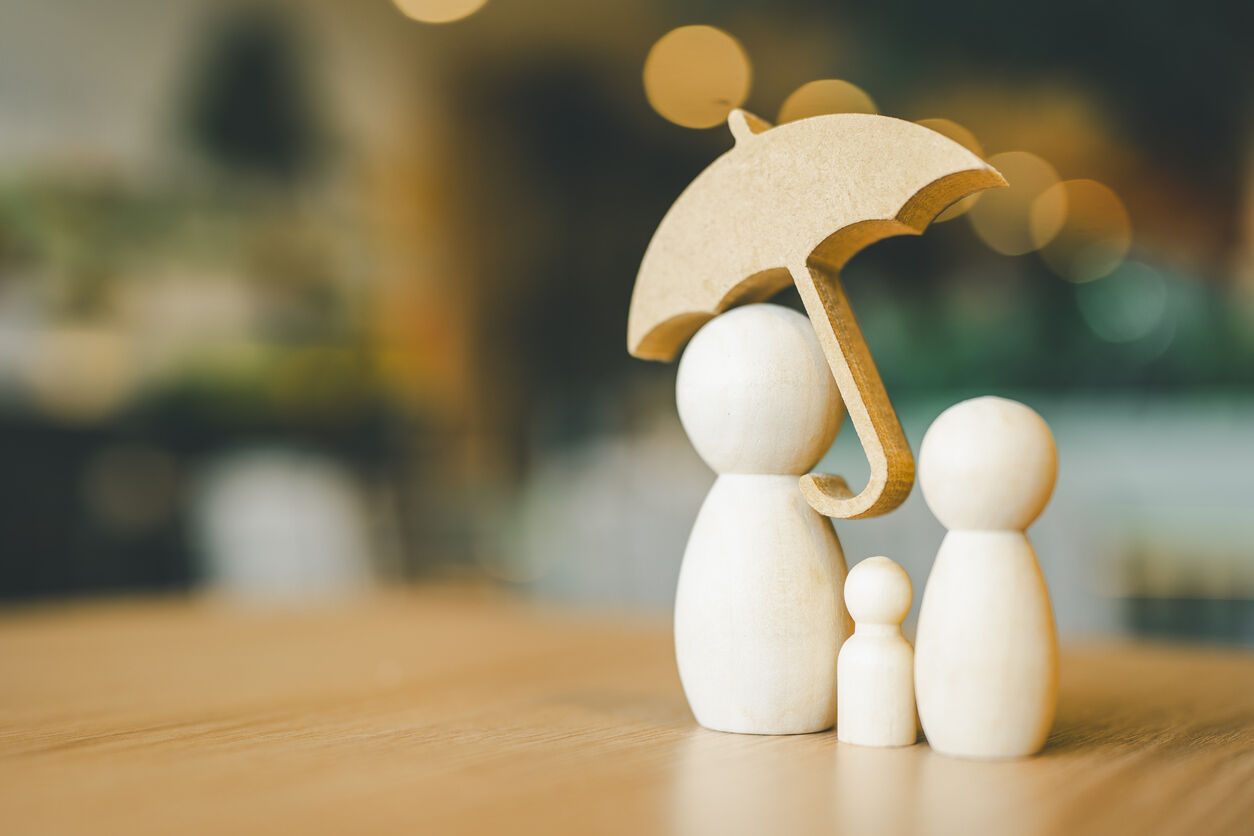 Wooden family figurines under an umbrella, symbolizing protection, representing the theme of hiring a life insurance attorney.