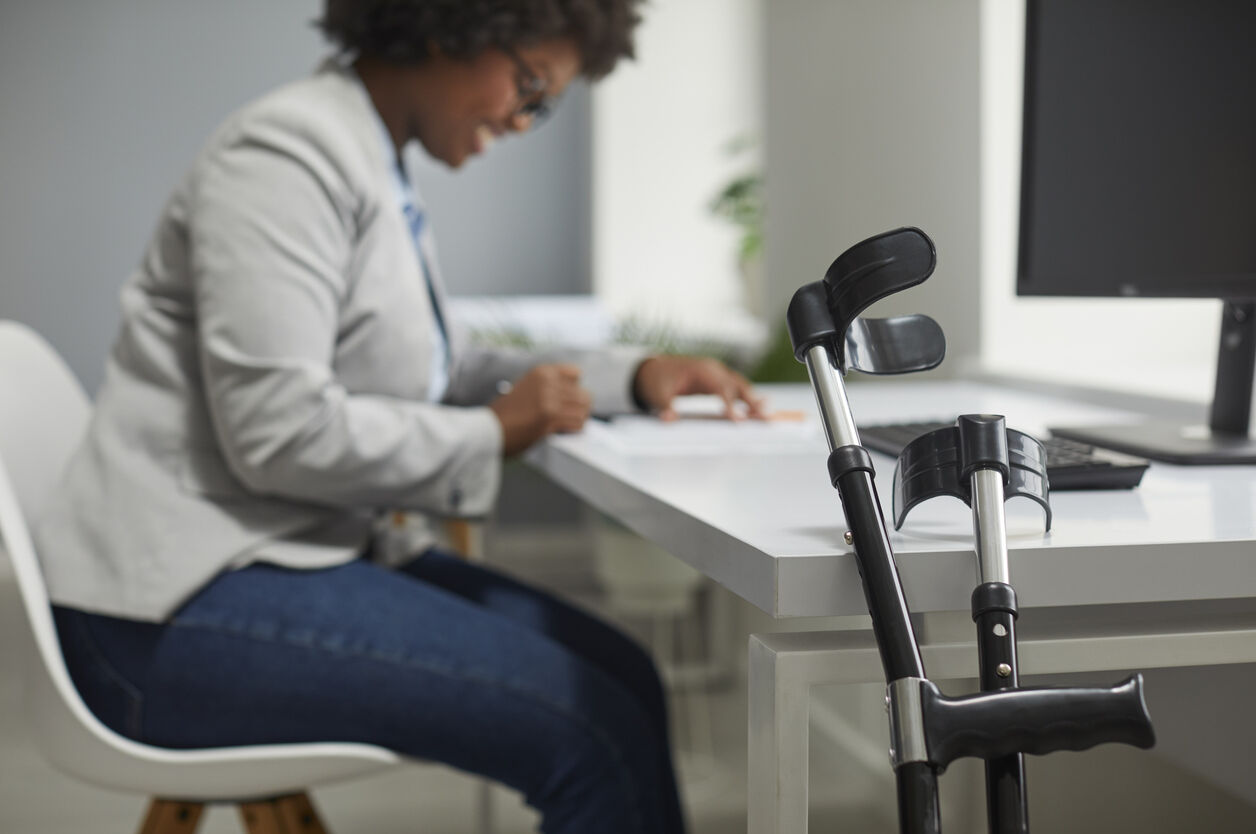 A professional working at a desk with crutches nearby, highlighting the relevance of disability insurance for lawyers and licensed professionals.